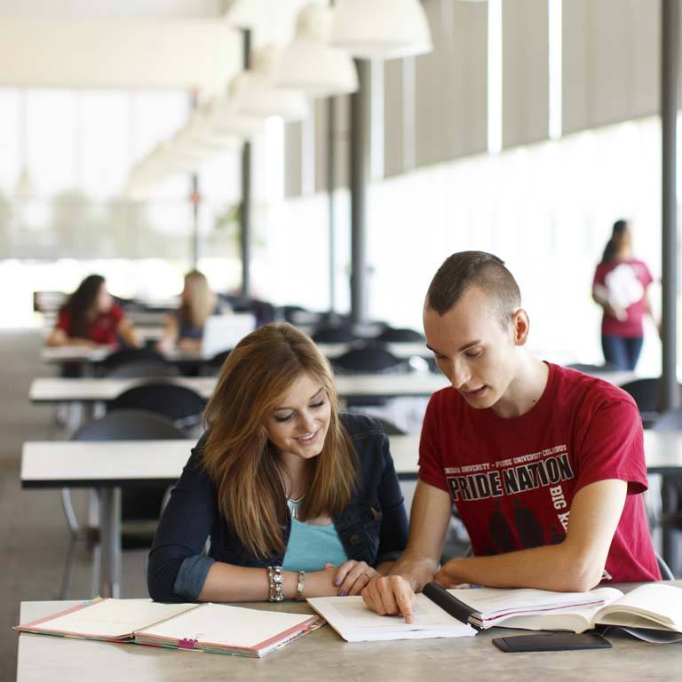 Two people sit at a table looking at a book on the Indiana University Columbus campus